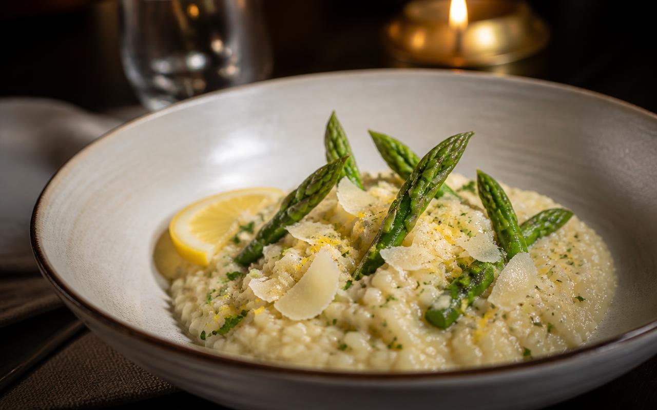 A bowl of creamy risotto flecked with fresh herbs and lemon zest, topped with roasted asparagus spears and shaved Parmesan